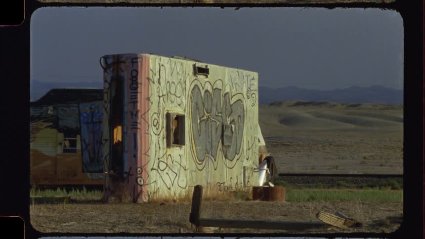 A graffiti-covered abandoned structure sits alone in a desolate desert landscape during golden hour