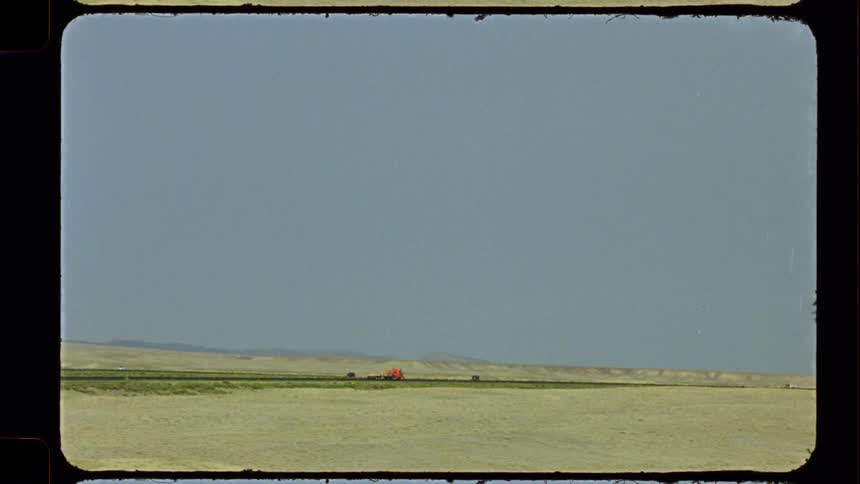 Vintage 8mm film captures a wide, desolate landscape with cars and trucks driving along a distant highway