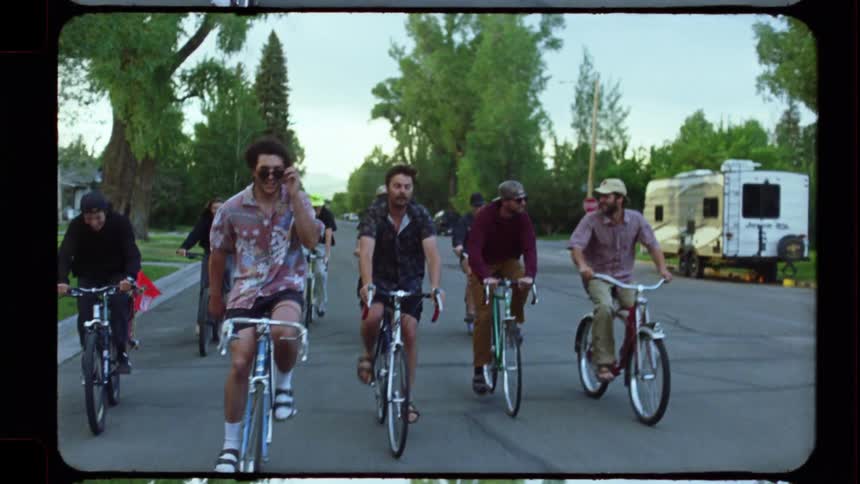 A group of male friends ride together on their bicycles down a quiet neighborhood street in this vintage film-style clip