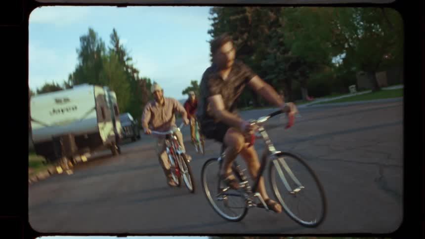 Vintage film footage captures a group of friends riding their bikes through a suburban neighborhood at sunset