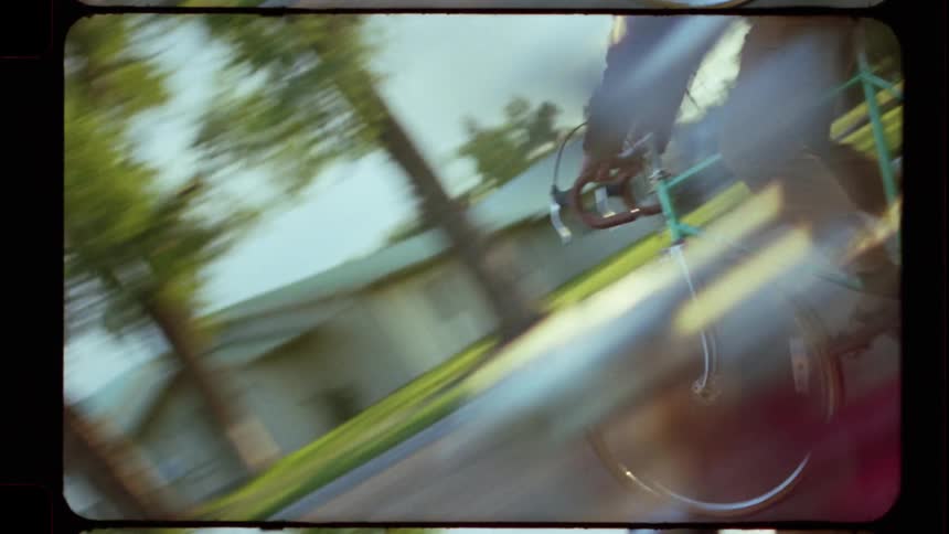 Vintage 8mm film captures a group of friends riding bikes together down a suburban street at sunset