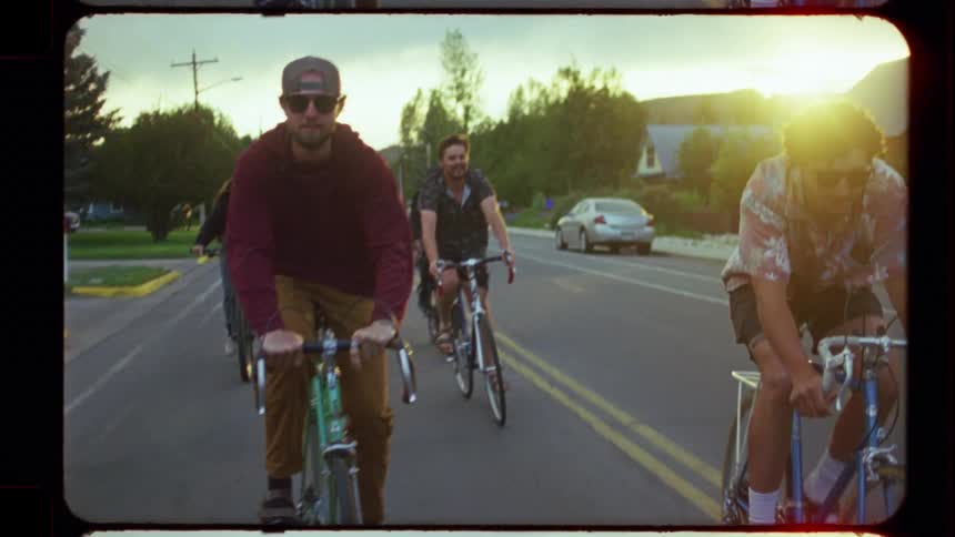 A group of friends enjoys a leisurely bike ride together through a neighborhood street at sunset, captured in a vintage film style