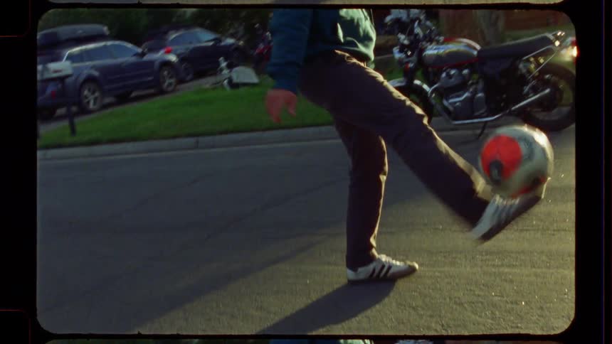 A young man skillfully juggles a soccer ball on a suburban street in a nostalgic, slow-motion shot captured on 16mm film