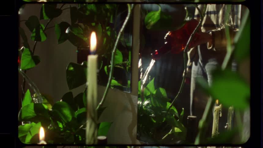 Vintage-style footage captures a quiet moment of a person watering houseplants by the warm glow of candlelight