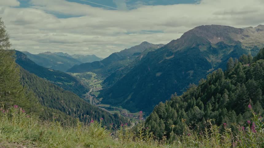 Wide scenic shot of a lush green mountain valley with a small village below under a cloudy sky
