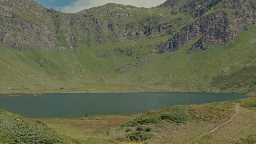 A serene mountain lake sits peacefully in a lush green valley surrounded by towering mountains on a sunny day