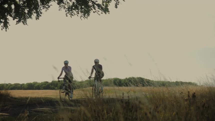 Two female cyclists ride along a scenic country path in slow motion on a beautiful sunny day