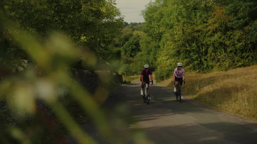 Two women enjoy a leisurely bike ride along a picturesque, tree-lined country road