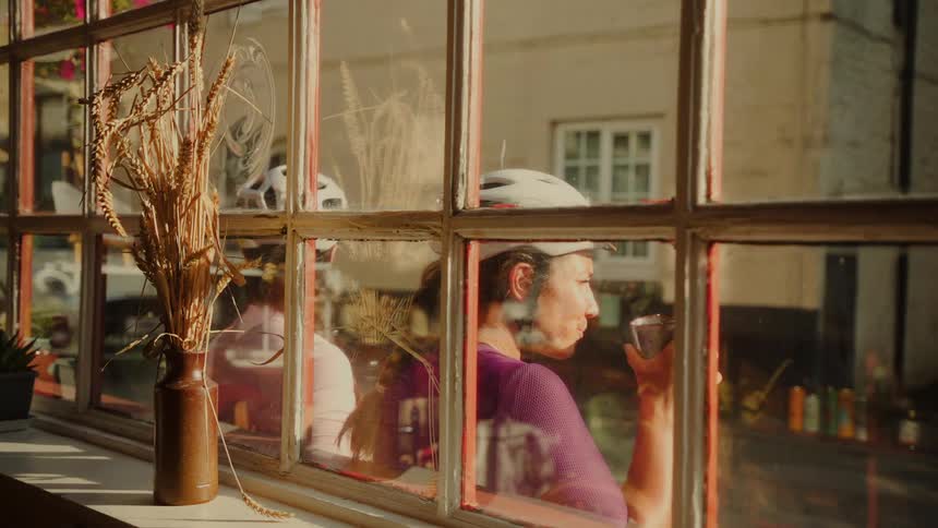 Two women in cycling gear enjoy a relaxing break by a sunny window inside a cozy cafe