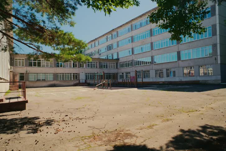 Static wide shot of a deserted schoolyard in front of an old, multi-story building on a bright sunny day