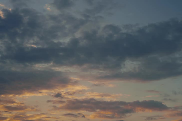 A tranquil evening sky painted with dark, dramatic clouds and the warm, fading light of a sunset