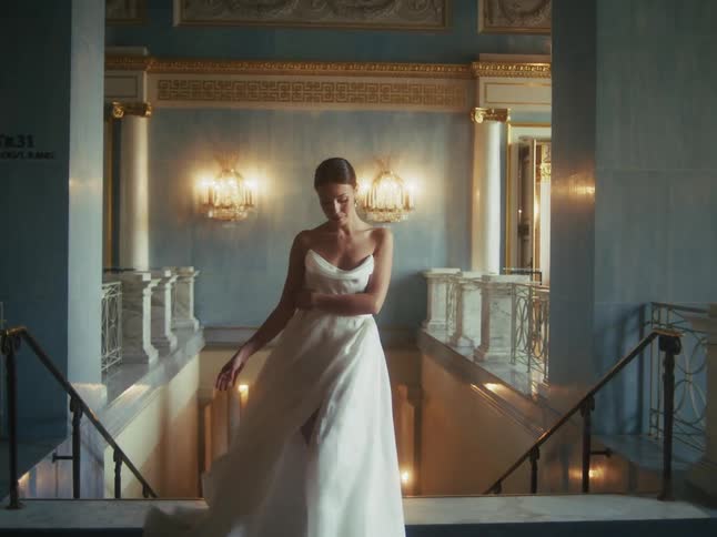 An elegant woman in a beautiful white gown twirls gracefully before posing at the top of a grand staircase