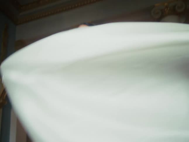 A beautiful woman in a flowing white gown dances in slow motion through an opulent, historic ballroom