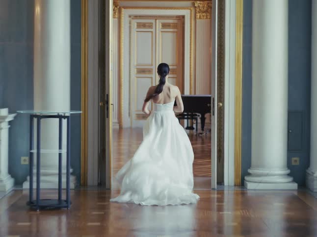 A beautiful bride in a flowing white gown gracefully walks away through the ornate halls of a grand palace, turning back to give a joyful smile