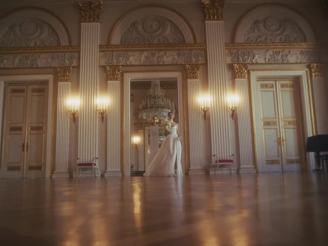 An elegant bride in a stunning white gown walks through a grand and luxurious palace ballroom