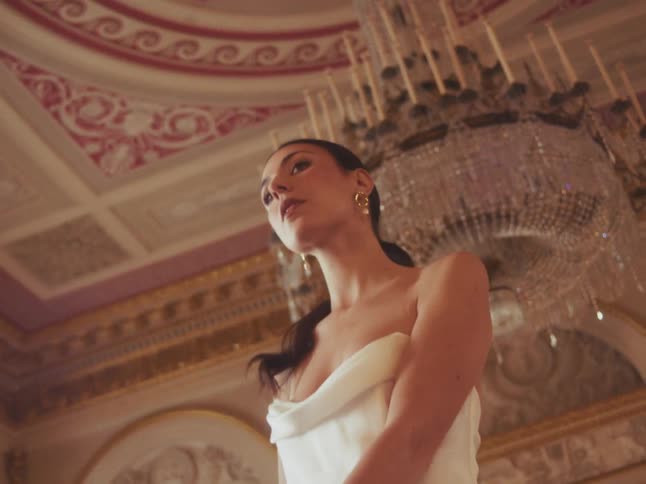 Low-angle slow-motion shot of a beautiful bride in a white gown dancing and smiling at her partner in a magnificent ballroom under a crystal chandelier