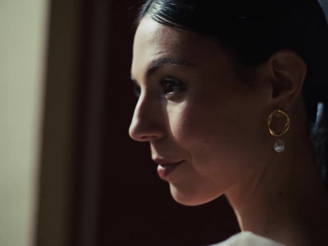 An elegant bride in soft light holds a bouquet of white roses and looks thoughtfully towards the camera