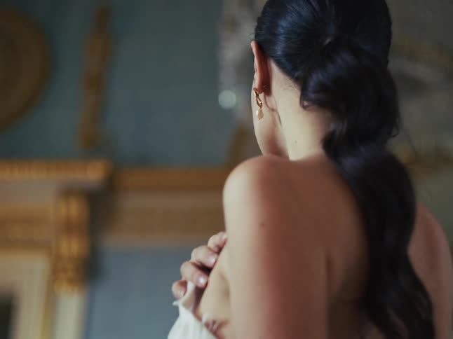 A beautiful, elegant woman with pearl earrings gazes thoughtfully in a luxurious, classic-style room