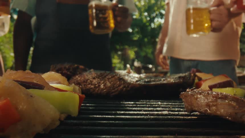 A sizzling steak is flipped on the grill before the camera pulls back to reveal friends toasting their drinks at a sunny backyard barbecue