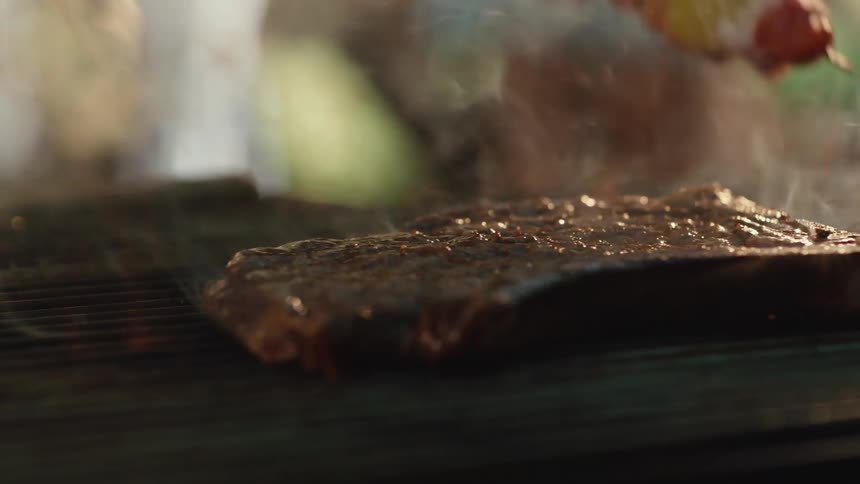 A juicy steak and vegetable kebab sizzle in slow motion on a fiery barbecue grill, with smoke billowing around them