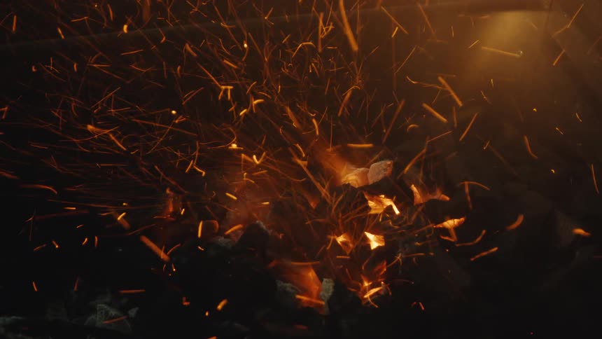 A mesmerizing slow-motion close-up of fiery sparks erupting from burning charcoal embers