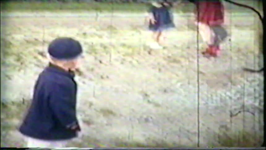 A man holds a little boy and girl together in a grainy, vintage home movie