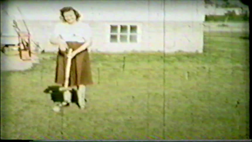 A smiling woman in vintage attire plays a game of croquet in her grassy backyard in this archival home movie from the 1940s