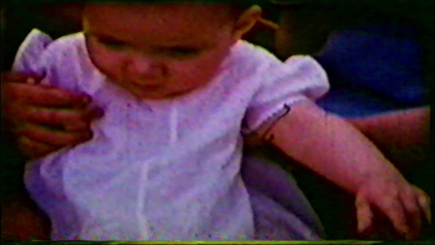 Archival close-up shot shows a cute baby being held by an adult in a vintage home movie