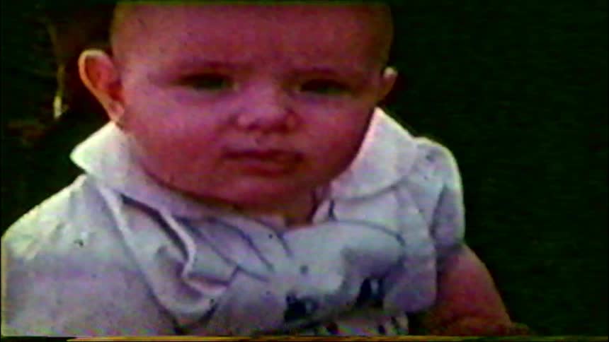 A close-up of a baby's face from a grainy and color-saturated vintage home movie