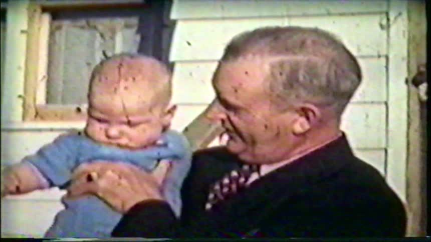 Vintage footage shows a mother and grandfather lovingly holding a baby boy outside their home in the 1940s