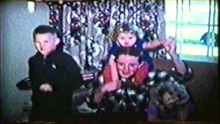 Playful siblings smile and wave for the camera in a grainy vintage home movie from the 1950s
