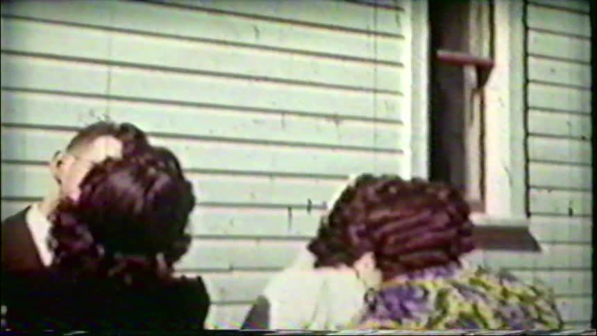 Friends and family congratulate a smiling man and woman with hugs and kisses in a vintage home movie from the 1940s