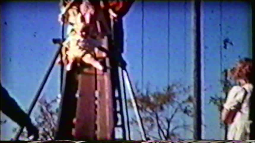 A nostalgic home movie shows a toddler being helped down a tall playground slide