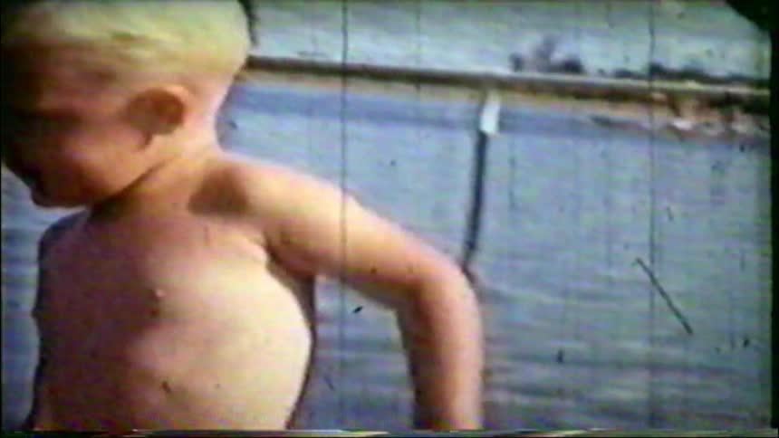 Vintage home movie of a blond toddler splashing and playing in shallow beach water on a sunny day