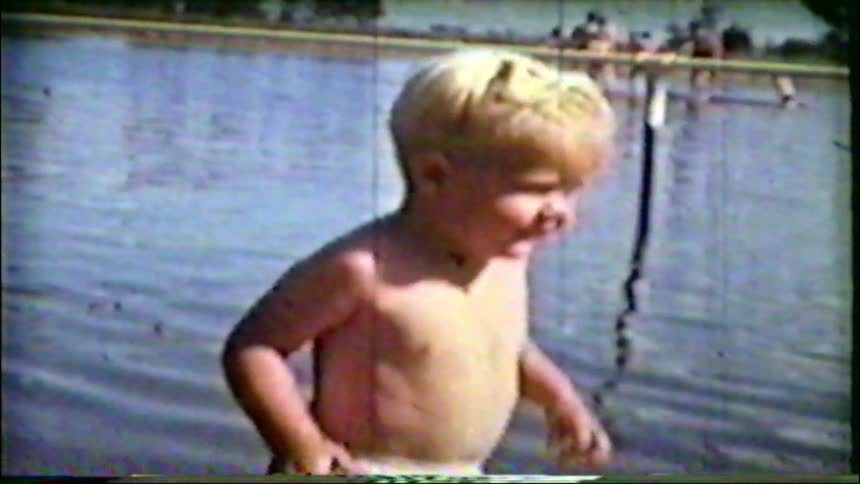 Vintage home movie captures a cute blonde toddler happily splashing in a lake on a sunny day