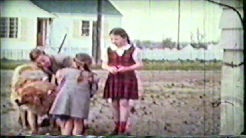 A sweet vintage home movie shows a group of children gathered around their fluffy dog in a suburban backyard