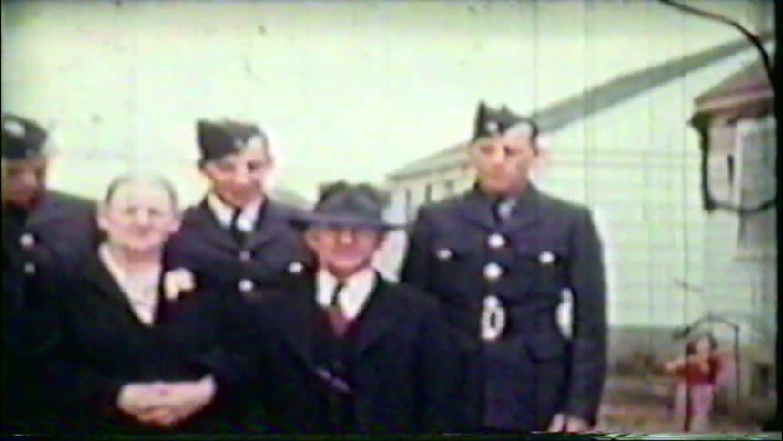 A vintage home movie captures a family portrait with parents and their sons in military uniforms