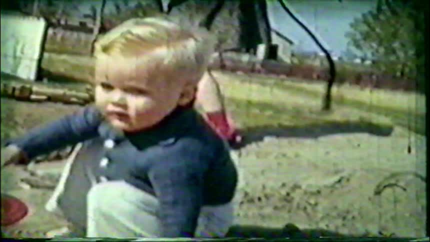 Nostalgic vintage footage shows a young blonde toddler playing in the dirt with his toys on a sunny day