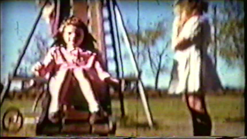A nostalgic home movie from the 1950s captures young girls in dresses having fun on a playground slide