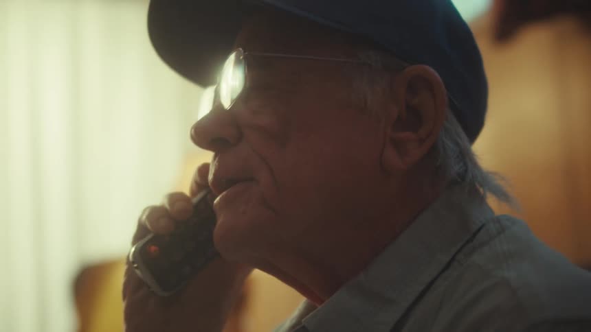 An elderly Air Force veteran with glasses smiles and then listens intently during a phone call in his home
