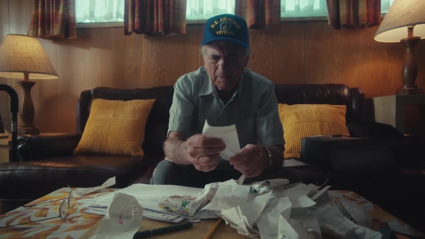 An elderly U.S. Air Force veteran sifts through a mountain of receipts while managing his finances in his living room