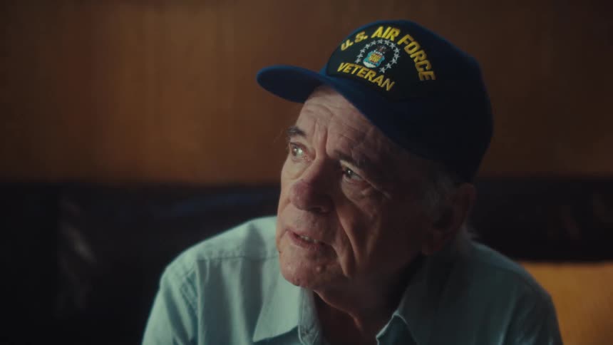A pensive elderly Air Force veteran sits quietly, reflecting on his past with a bittersweet expression