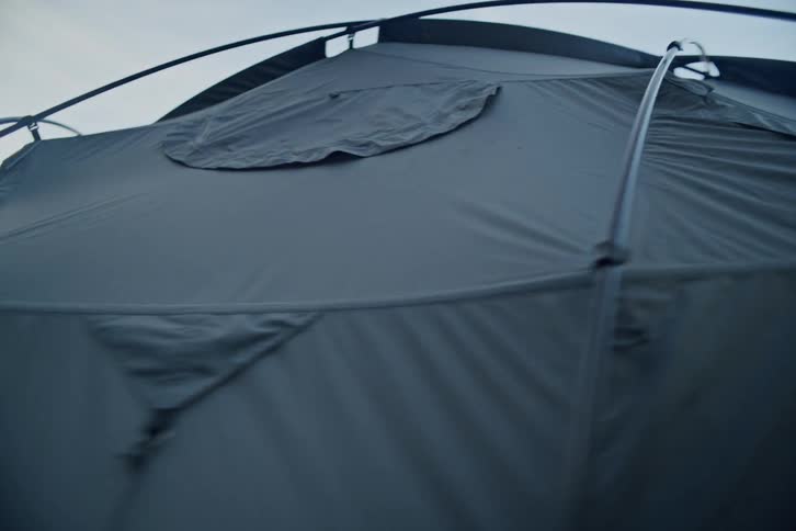 A slow-motion, low-angle pan reveals the details of a modern camping tent set up in a tranquil forest
