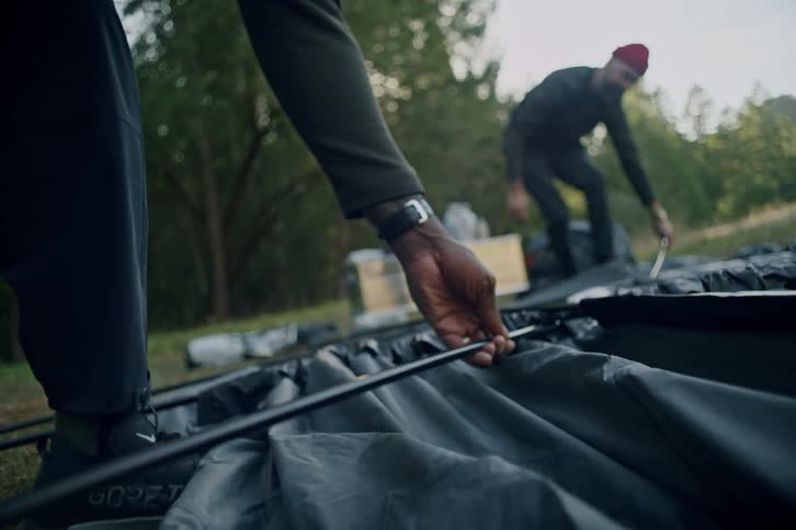 A close-up shot of two friends setting up a tent together in a serene forest clearing during their camping trip