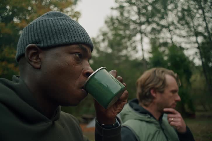 Slow motion close up of a man in a beanie drinking a hot beverage from a green mug at a campsite