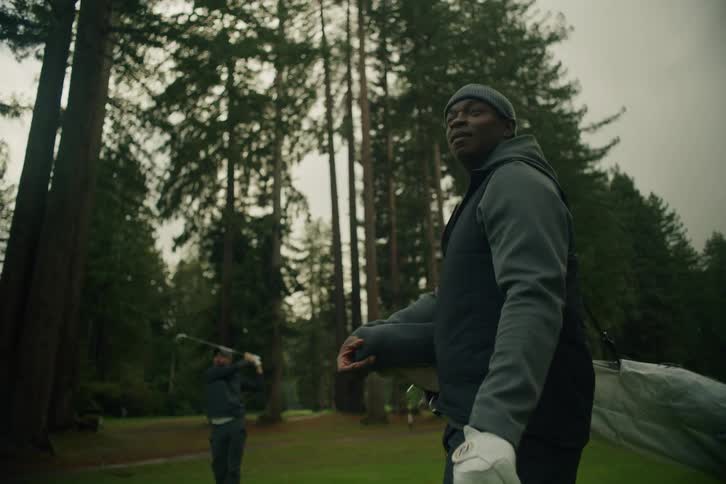 Two friends enjoy a game of golf on a scenic course surrounded by a forest of tall trees, with one man taking a swing in slow motion