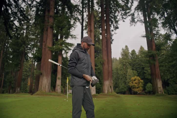 A golfer pulls a club from his bag and prepares to tee off on a stunning course amongst giant redwood trees