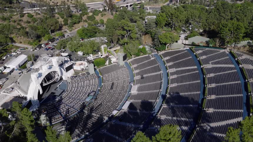 An aerial shot slowly pushes in and tilts down over the empty Hollywood Bowl amphitheater with the Los Angeles skyline in the background