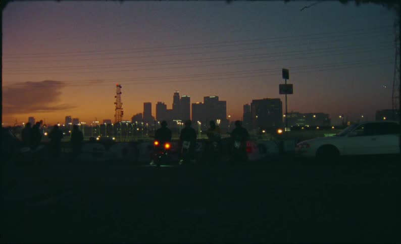A group of bikers on motorcycles are silhouetted against the downtown city skyline at sunset