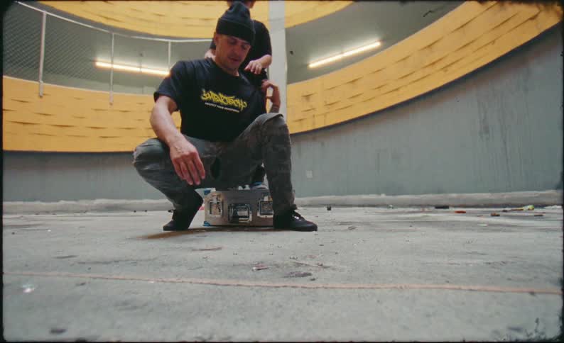 In an urban parking garage, a playful father puts a metal case on the ground so he can lift his smiling son onto his shoulders